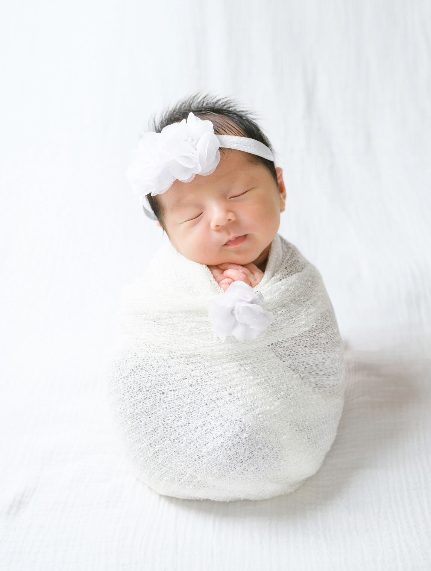 白い花のヘアバンドをつけ、白いおくるみで眠る赤ちゃん
