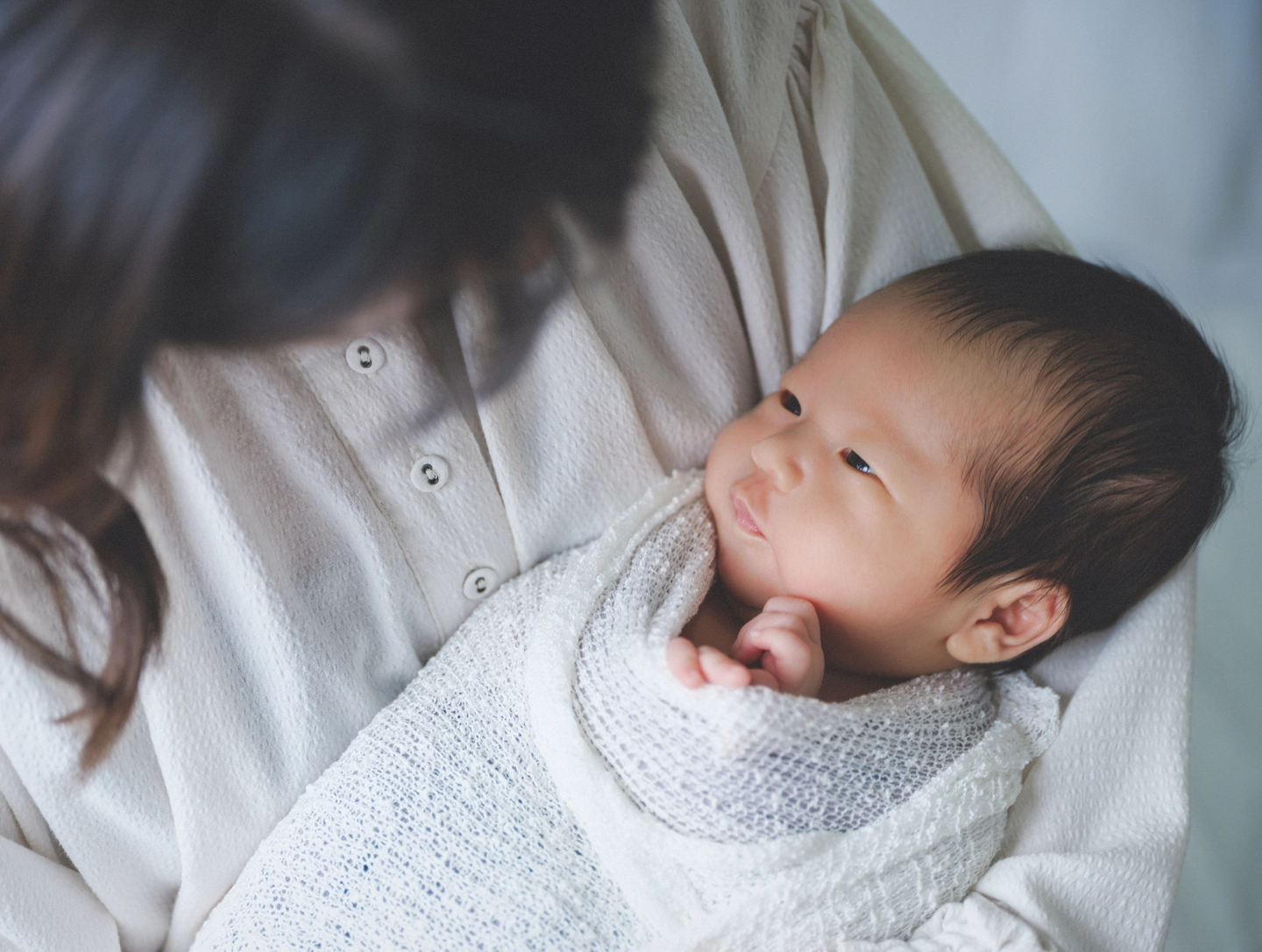 大人の腕に抱かれ、顔を見上げる赤ちゃんのニューボーン撮影例