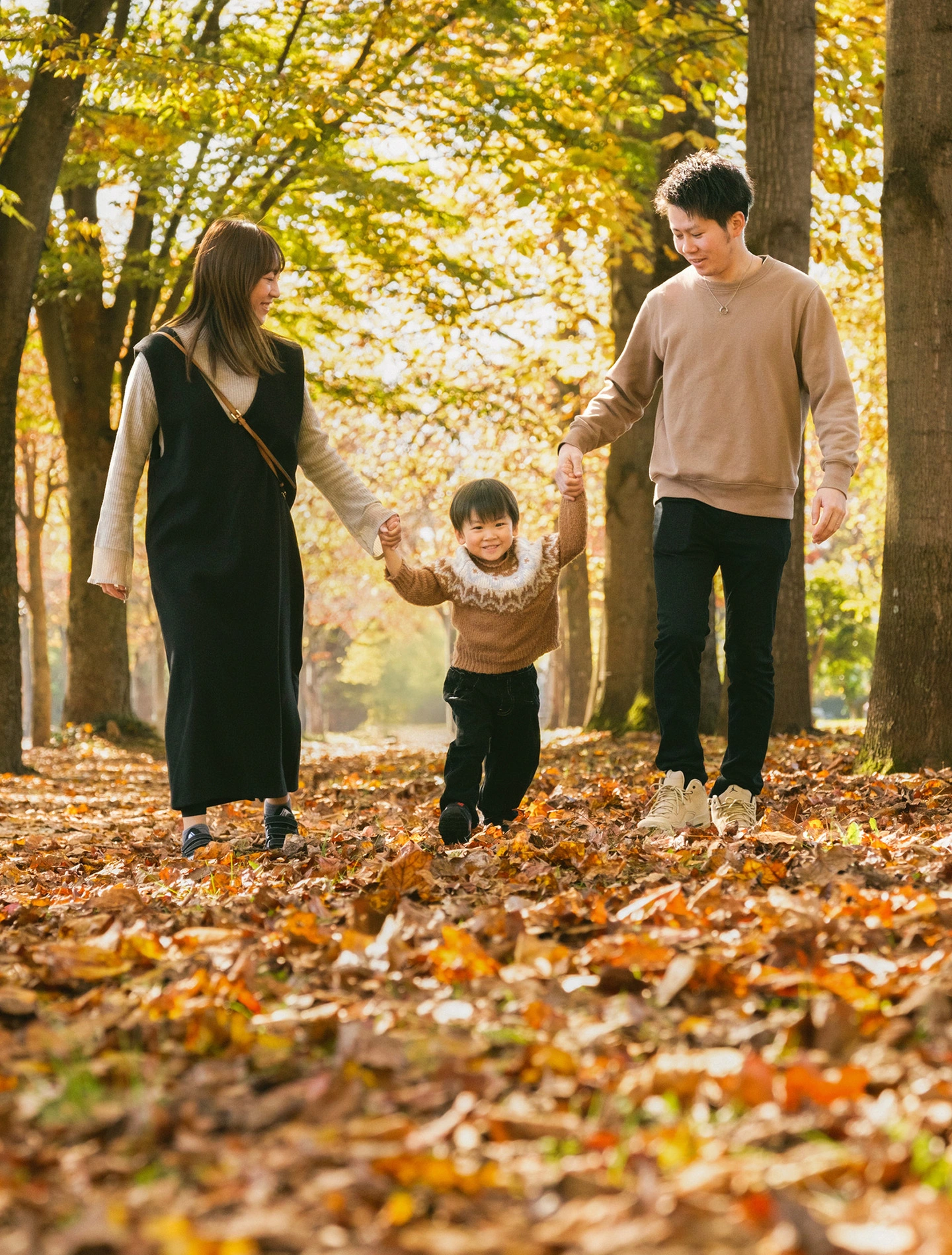 秋の木立の中で子どもと手をつなぐ両親