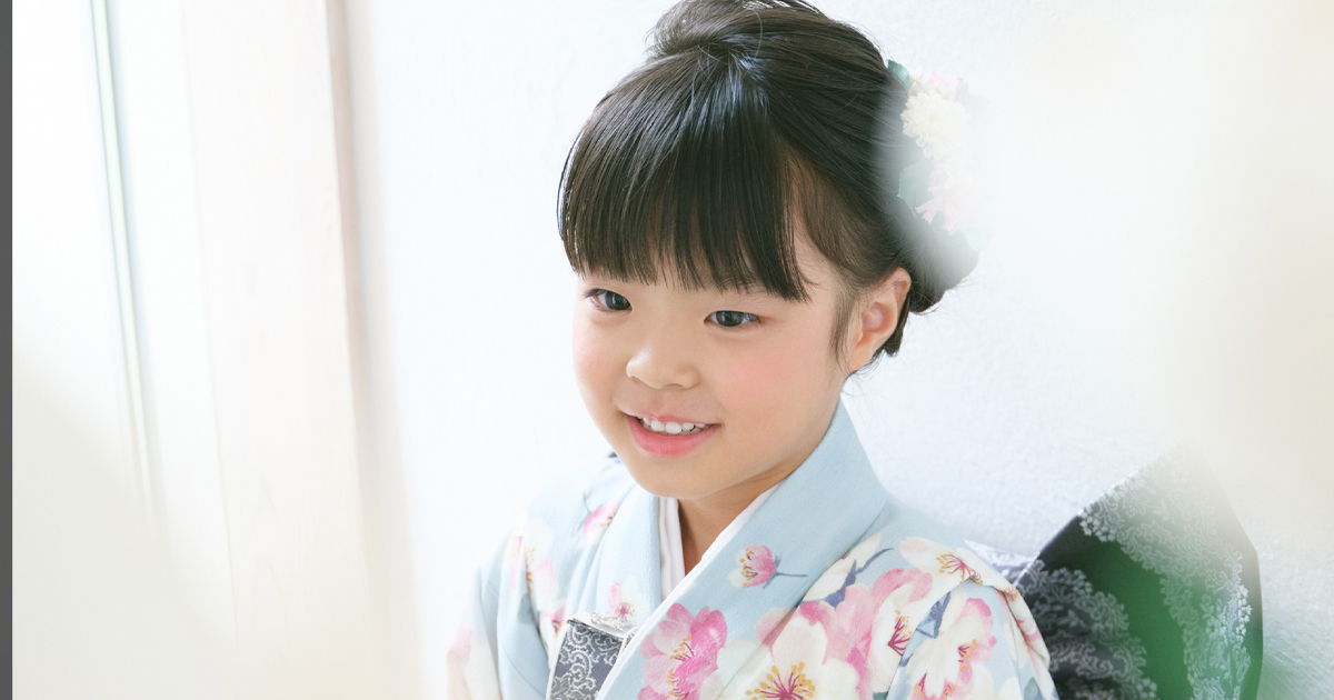 7歳女の子の七五三記念写真。淡い水色の着物姿で笑顔を見せる。佐直写真館にて。