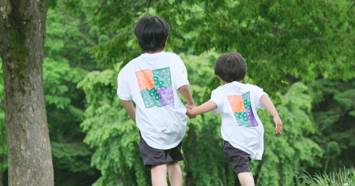 手をつないで走る兄弟の後ろ姿。緑の中で笑顔のロケーション撮影