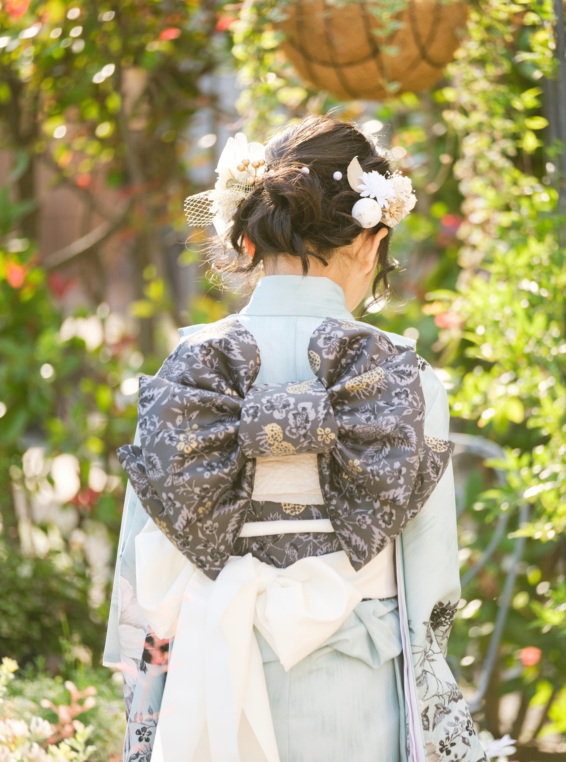 木漏れ日の中で帯結びと髪飾りを写した七五三の後ろ姿