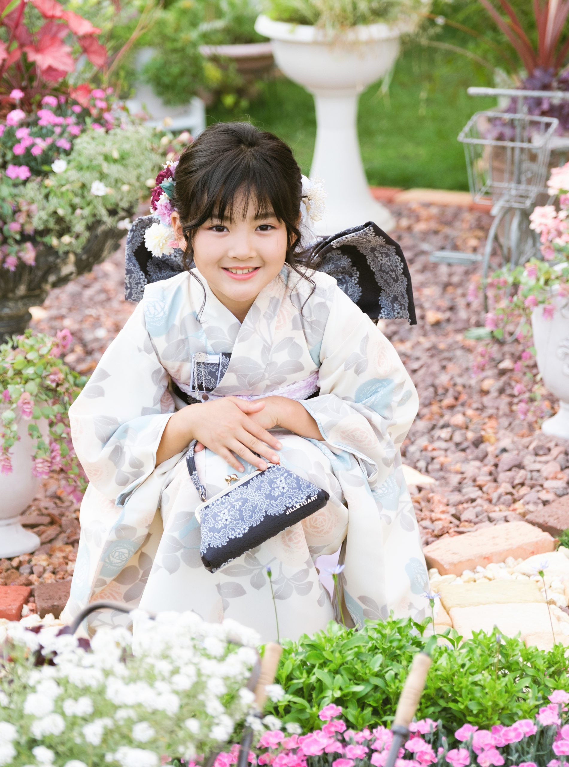 淡い色の着物で花に囲まれて座る7歳の七五三