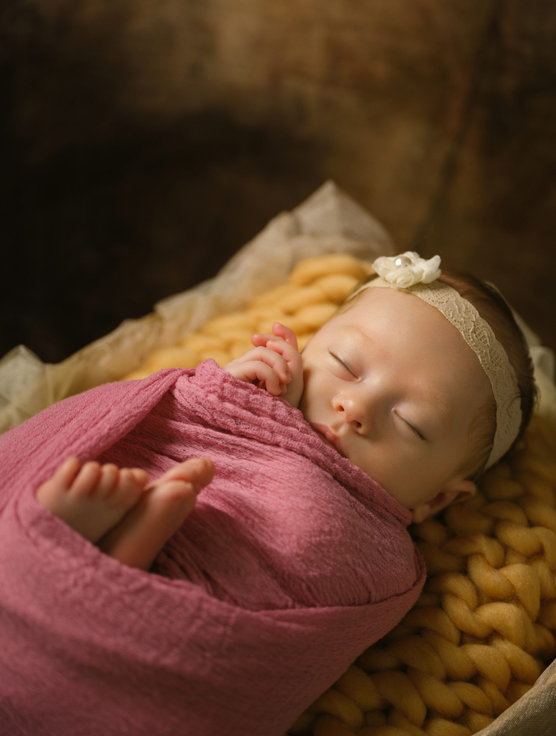 ピンクのおくるみと黄色のブランケットに包まれて眠る赤ちゃん