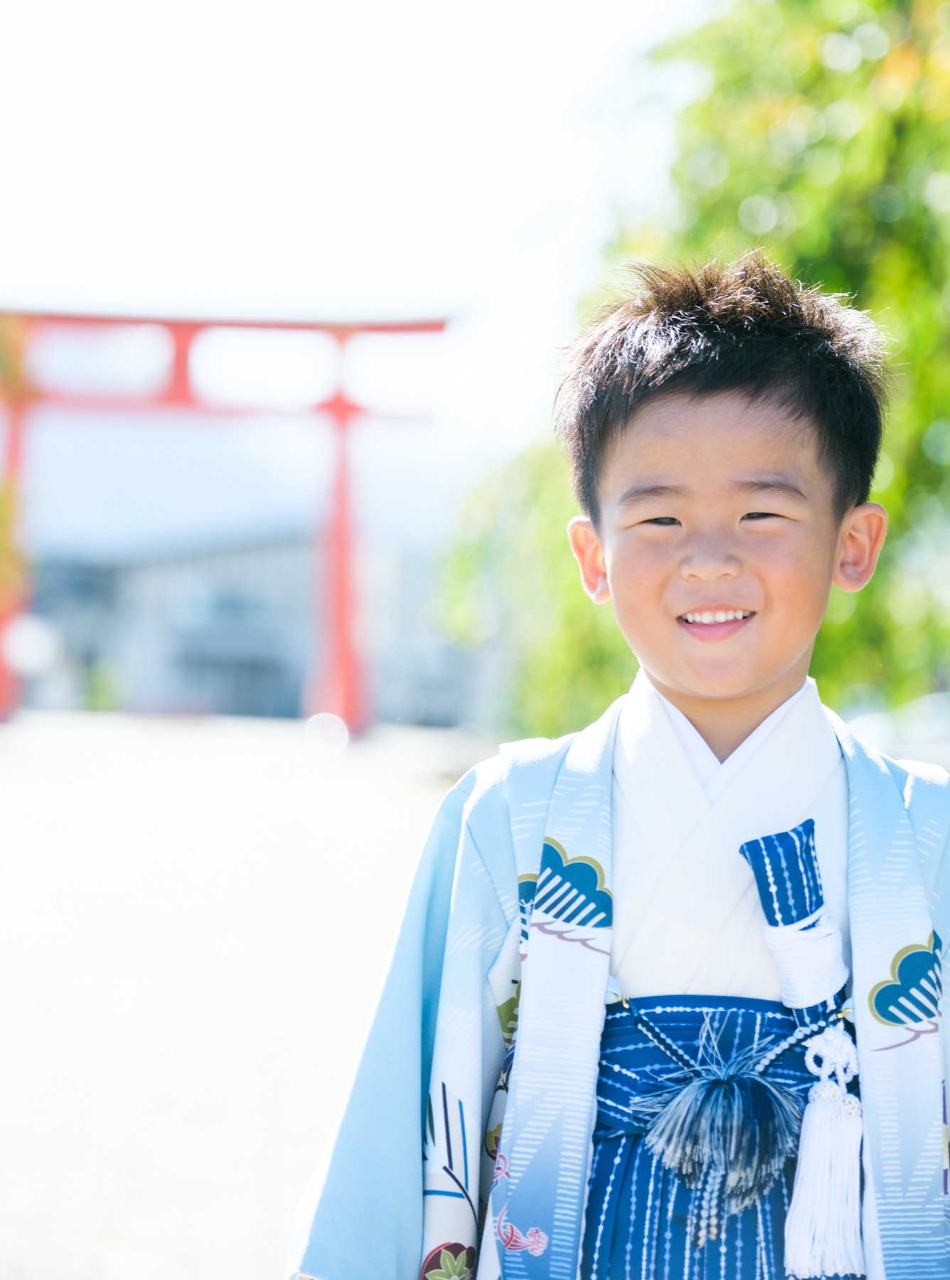 赤い鳥居と緑を背景に、にっこり笑う5歳の七五三