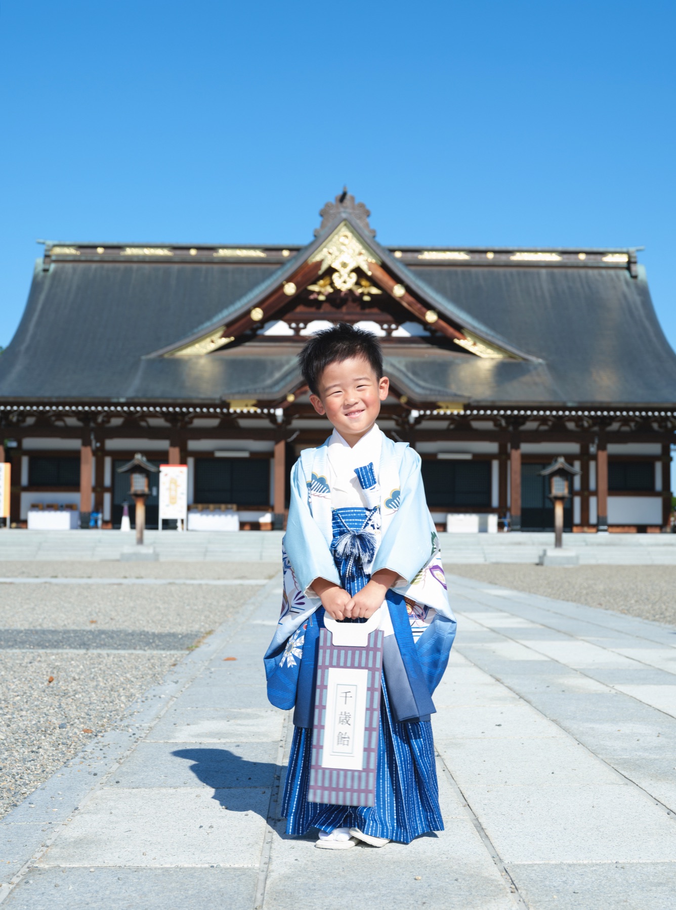 護国神社の社殿前で千歳飴の袋を持つ、水色の羽織袴姿の男の子