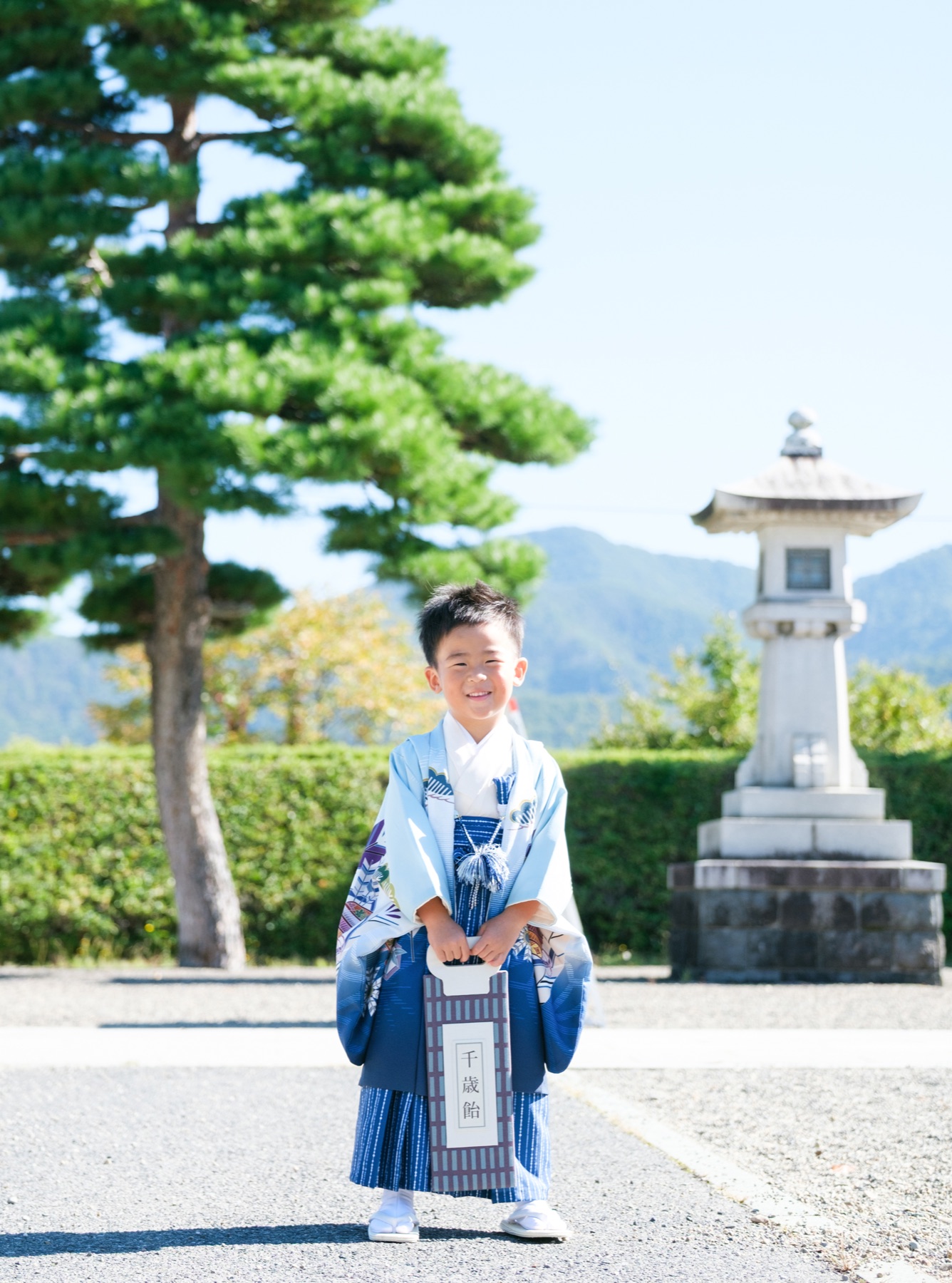 松と石灯籠を背景に千歳飴を持って立つ5歳の男の子