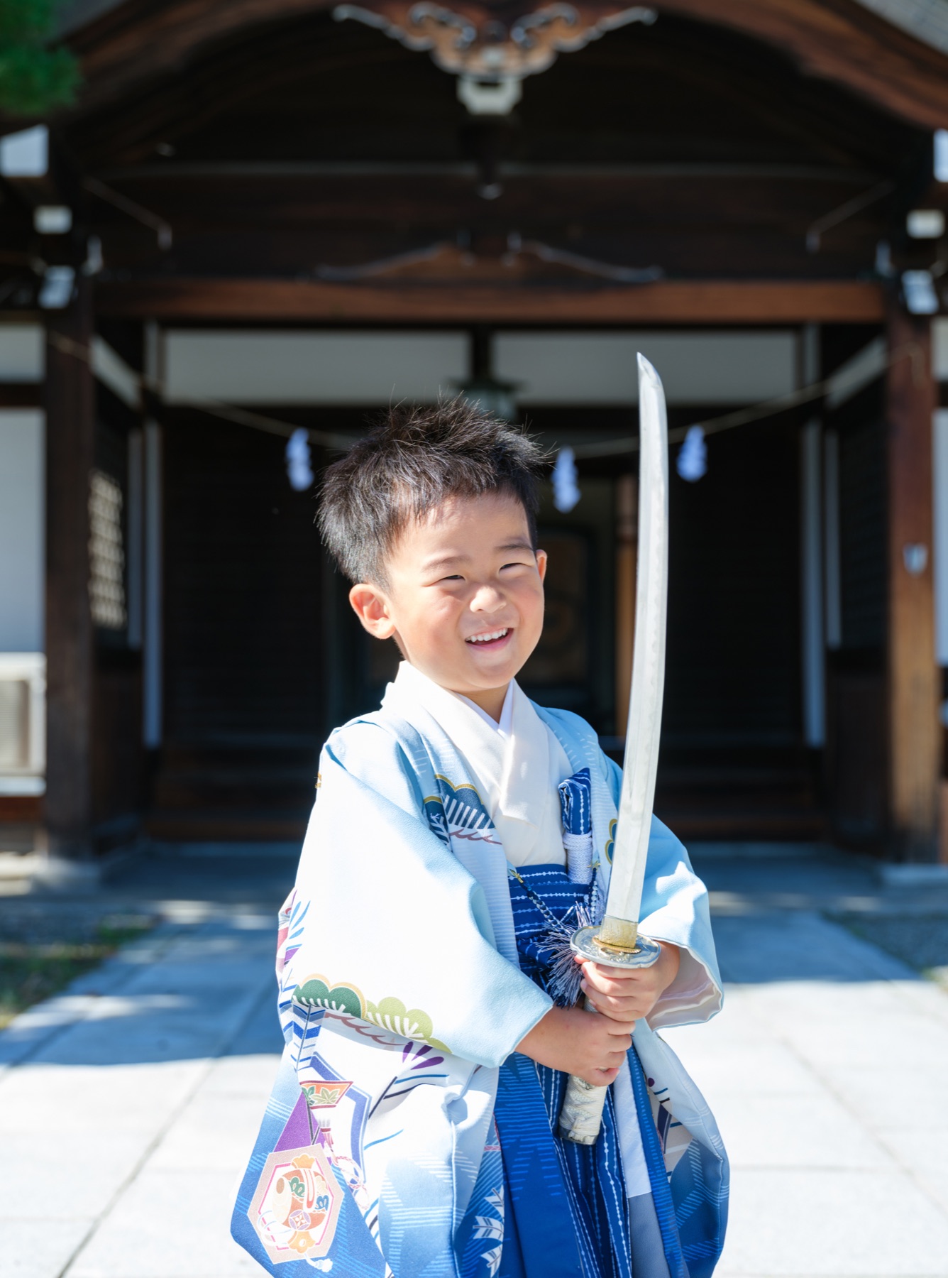 社殿の前で刀を持ち、明るく笑う七五三の男の子