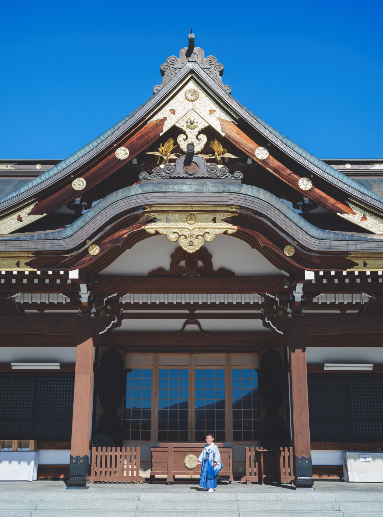 青空の下、護国神社の大きな社殿と5歳の晴れ姿